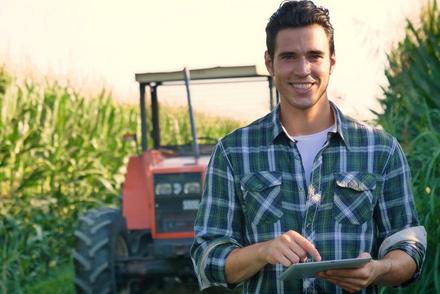 Junger Mann steht auf Maisfeld vor Traktor