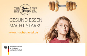 Gesund essen macht stark! Ein Mädchen hält einen Teller mit einem Brotgesicht und verschiedenem Obst und Gemüse in der Hand