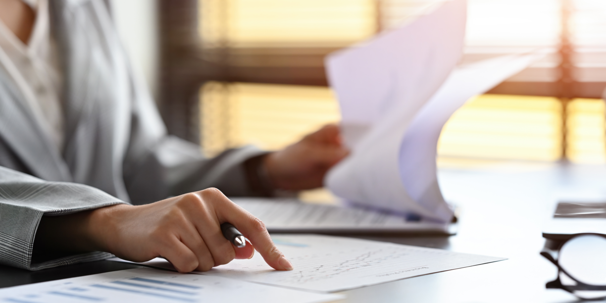 Bildausschnitt einer Person beim Lesen von Dokumenten an einem Schreibtisch