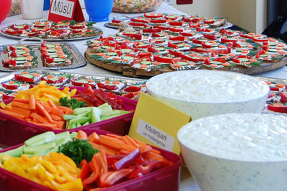 Auf einen Tisch stehen mehreren Schüsseln gefüllt mit Obst, Gemüse und Quark, Teller mit Brotgesichtern und weitere gesunde Leckereien