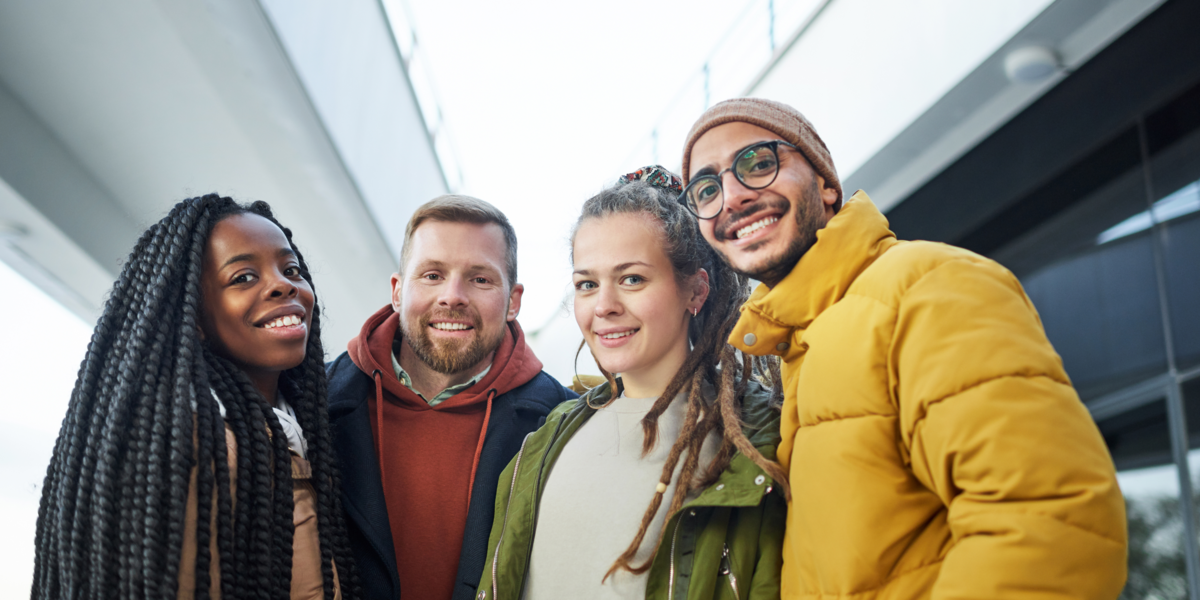 Vier junge Menschen unterschiedlicher Herkunft, die lachend in die Kamera blicken.